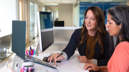 Two women reviewing something on a laptop in an office setting.